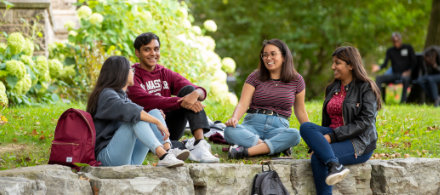 Four students sit on rocks in front of an old campus building